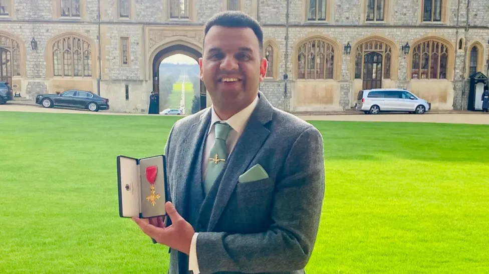 The image shows a man called Clive Lawrence holding his OBE medal